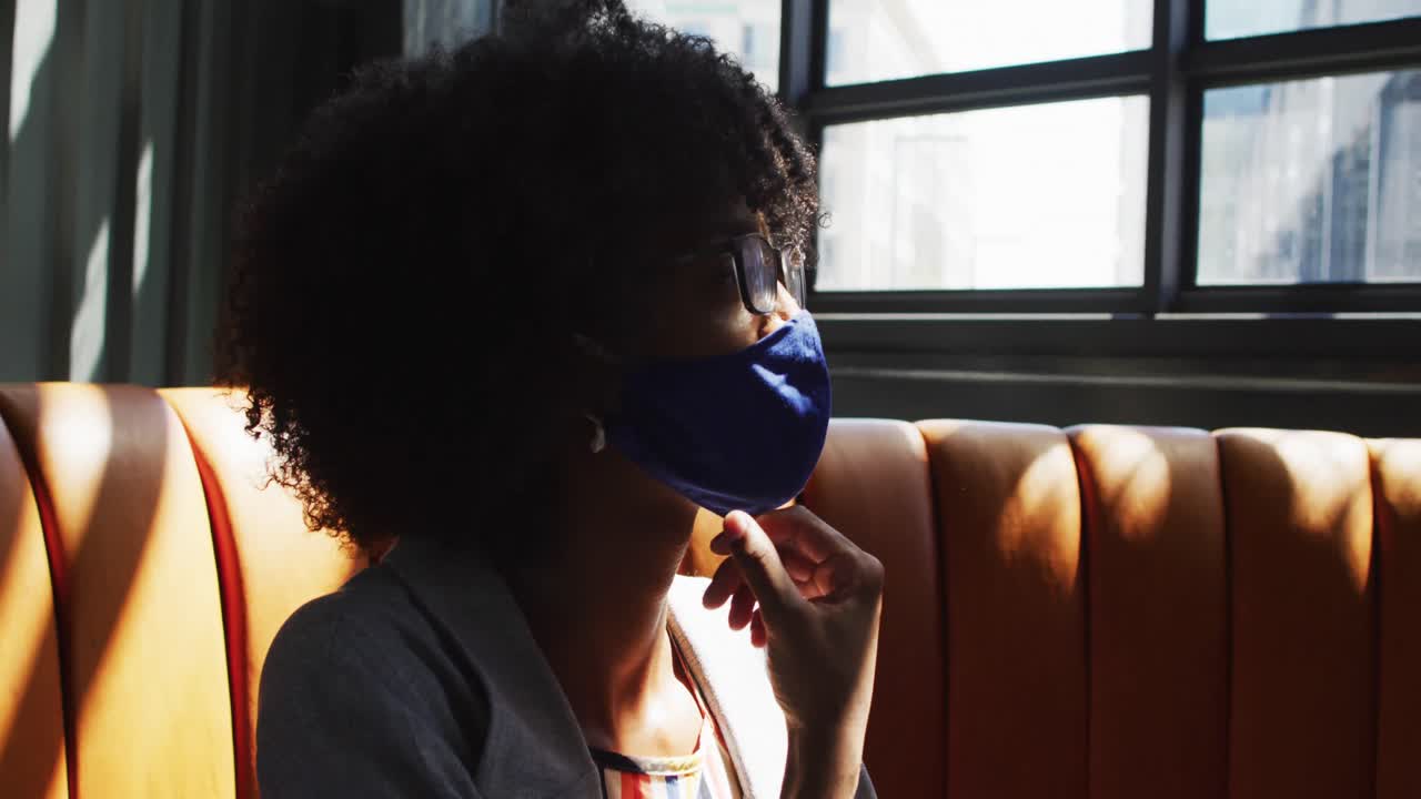 African american woman wearing face masks sitting in cafe looking at window