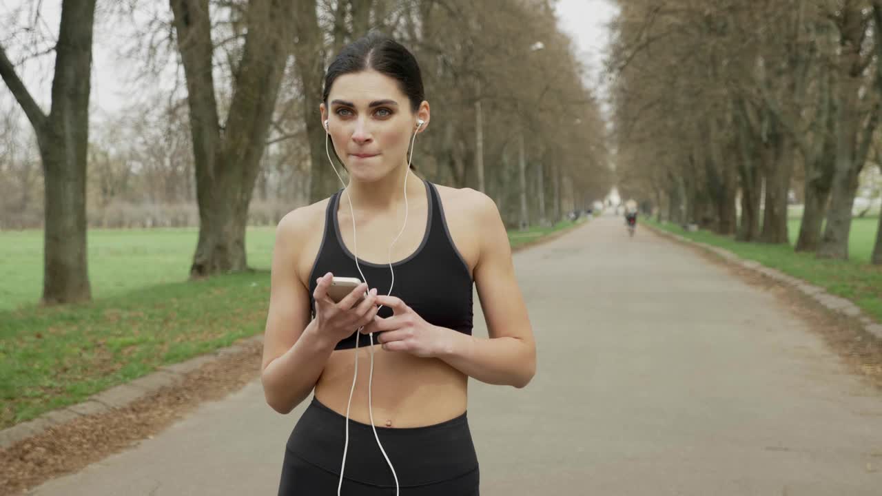 Young fsport girl is watching her smartphone, turning on music, running, healthy lifestyle, sport conception, communication concept