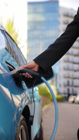 vertical video person charges an electric car at a station, connecting the charger and waiting. illustrating convenience and ecofriendliness of electric cars