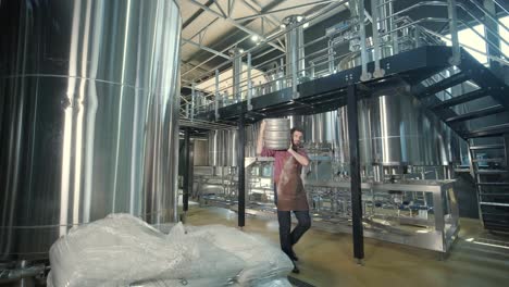 un joven cervecero con un delantal de cuero lleva un barril de cerveza artesanal en una cervecería moderna