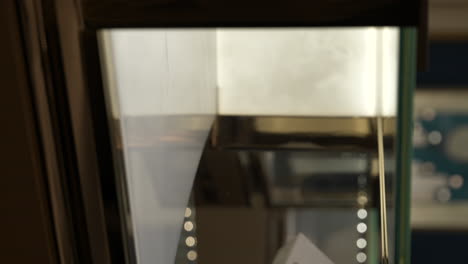 manos verticales que toman el caro reloj baume mercier de la exhibición de la joyería de vidrio