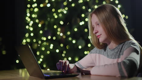 a teenage girl uses a laptop on the background of a christmas tree