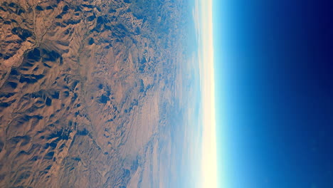 planet earth viewed from window seat, blue atmosphere and vivid orange rocky mountains