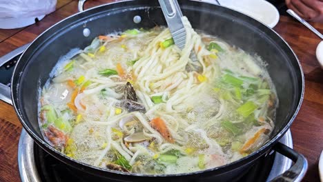 tongs mix knife cut noodle soup while cooking - seafood clam kalguksu boiling in pot