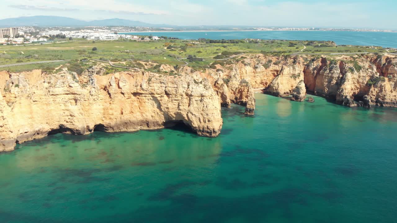Acantilados rocosos escarpados y agua esmeralda tranquila en Lagos, Algarve, Portugal - Toma aérea panorámica de establecimiento.