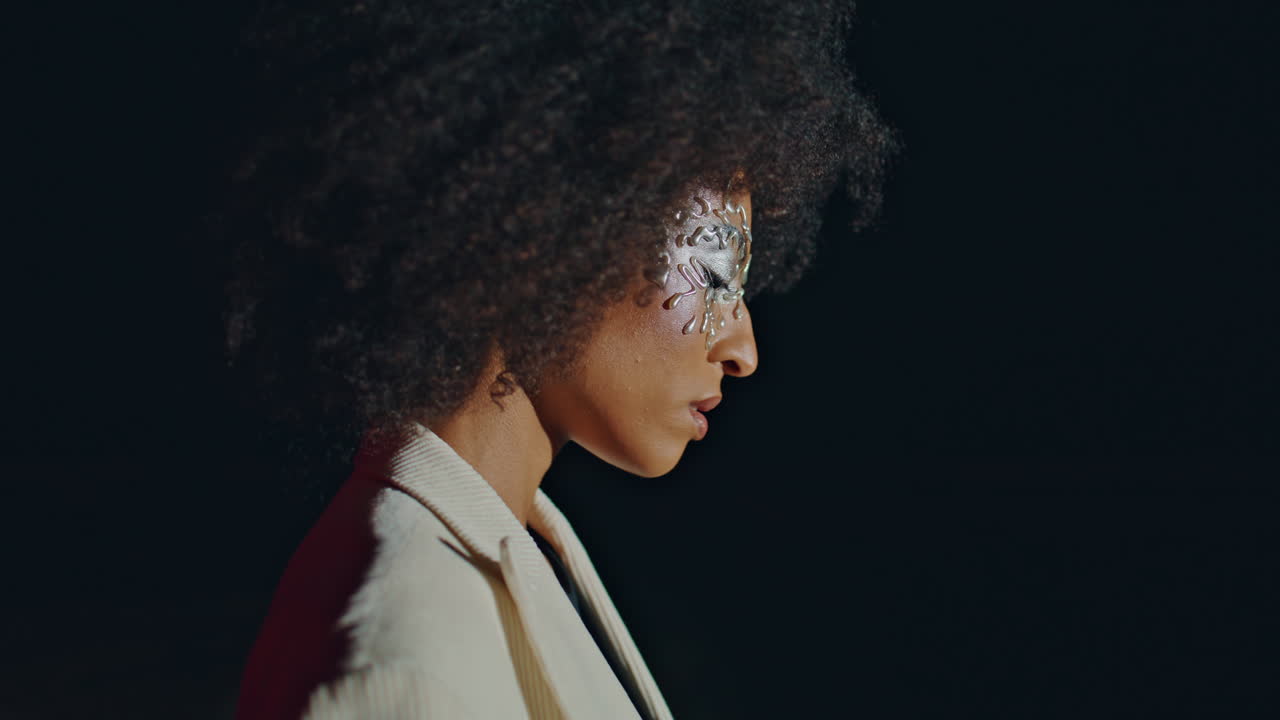 Modelo de moda en primer plano con fondo oscuro. Vista lateral de chica de fiesta con maquillaje artístico.