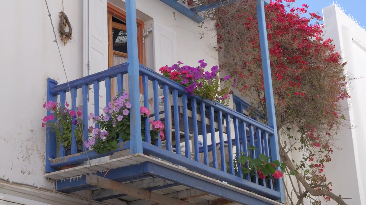 Pittoresco balcone blu con fiori rosa su un edificio bianco nelle Cicladi.