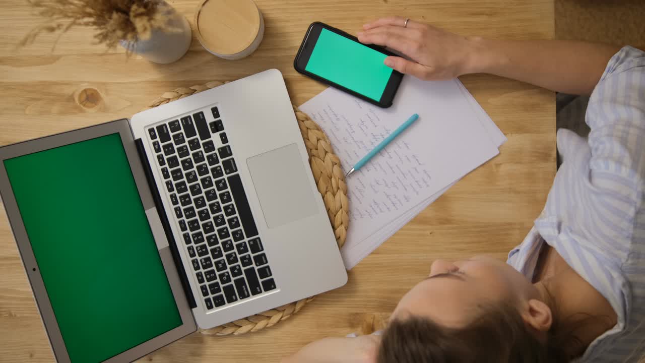 Green screen of the computer and phone. The girl is lying at the table and surfing the Internet. The concept of remote learning. Irresponsibility.