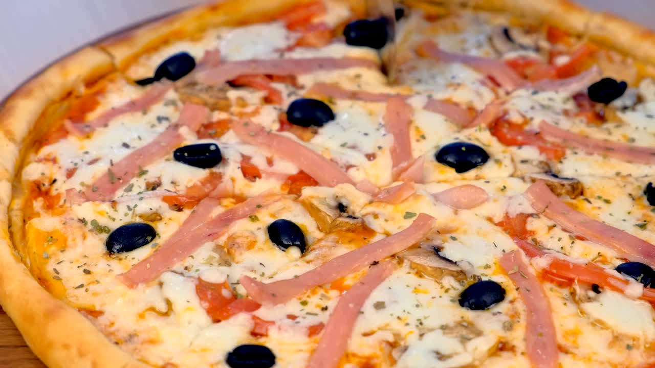 요리사는 테이블 위의 나무판에 베이컨과 치즈로 피자를 잘라줍니다.