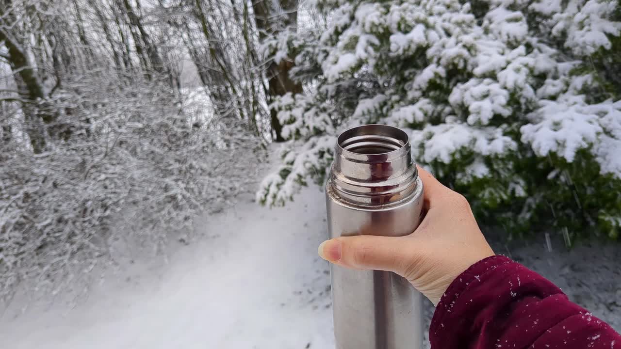 Woman holding hot drink thermos outside in nature on snowy winter day, close up