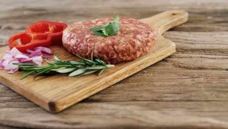 raw hamburger patty and ingredients on wooden board