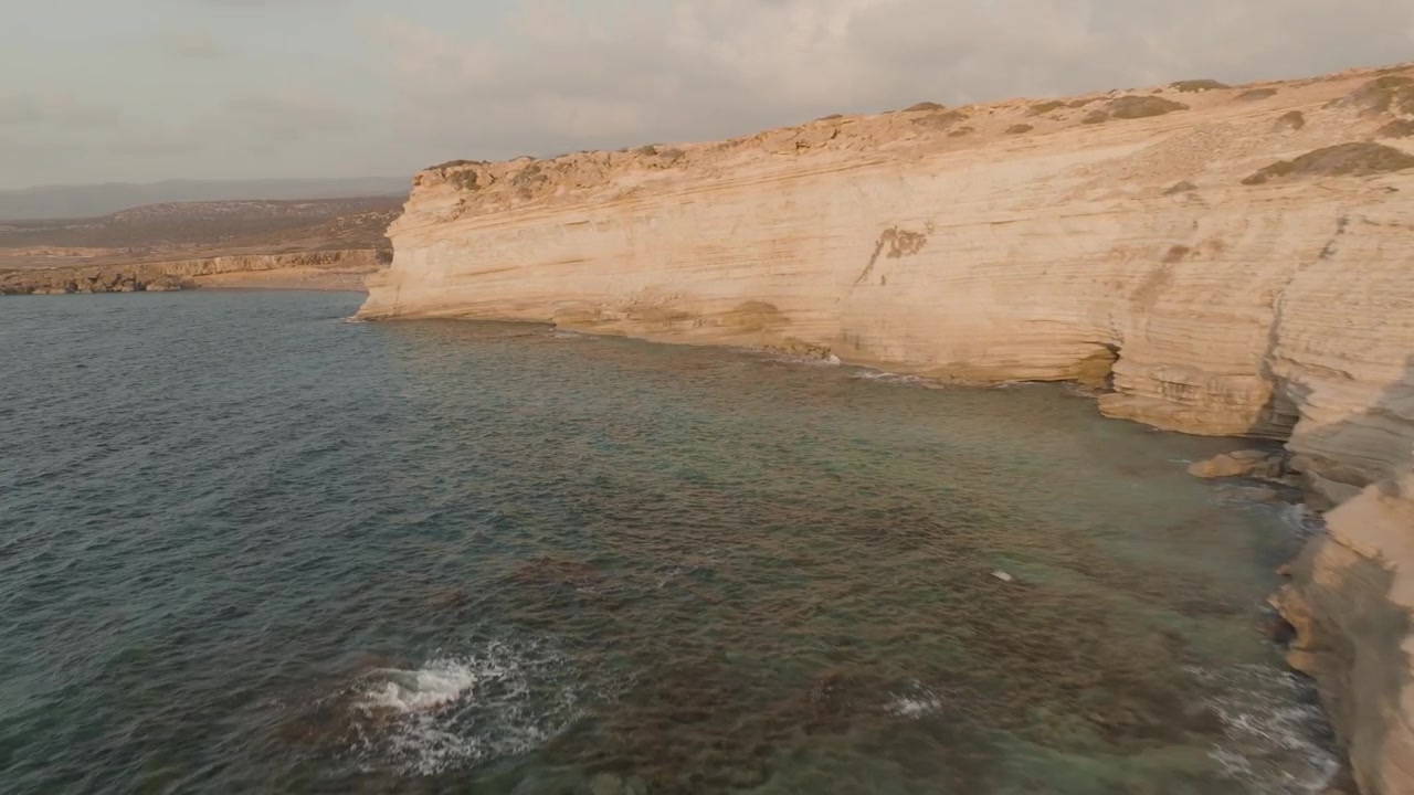 Riprese con drone di un'alta scogliera al tramonto a Cipro, con la luce dorata che evidenzia la costa frastagliata e le acque turchesi sottostanti, creando una scena naturale serena e mozzafiato
