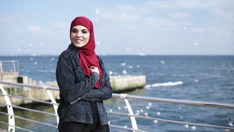 Young-muslim-girl-enjoys-walking-near-the-seaside-with-seagulls-flying-on-the-background