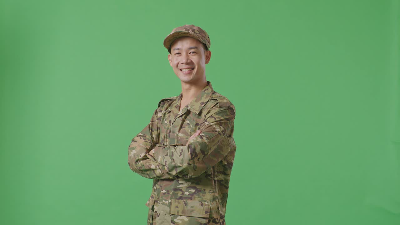 Side View Of Asian Man Soldier Smiling And Crossing His Arms While Standing In The Green Screen Background Studio