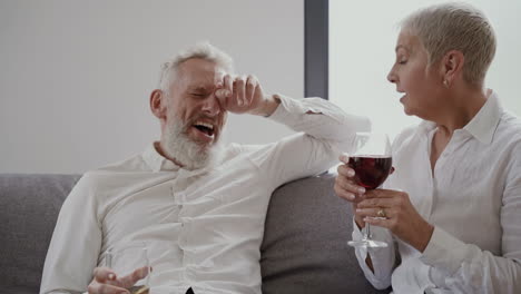 Mujer-Y-Hombre-Felices-Amigos-Mayores-Sentados-En-El-Sofá-Riendo-Y-Bebiendo-Una-Copa-De-Vino