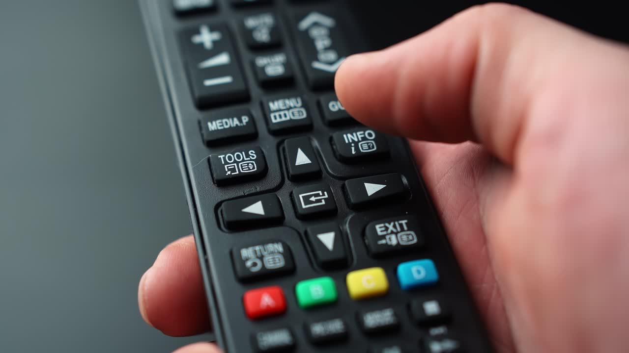 Close-up of a hand pressing the center OK Select button on a TV remote navigation pad, confirming a choice in an on-screen menu with shallow depth of field