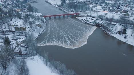 aerial establishing view of venta river rapids during winter flood, old red brick bridge, kuldiga, latvia, overcast winter day, wide drone shot moving forward tilt down