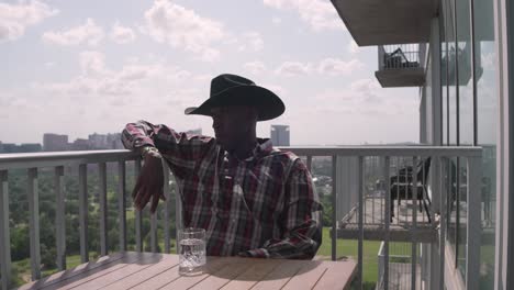 Portrait-shot-of-African-American-male-with-cowboy-hat-sitting-on-balcony