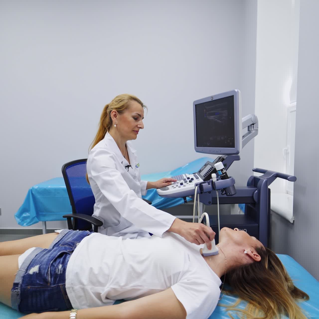 Large spacious doctor's cabinet for ultrasound examination. Doctor performing the thyroid gland checkup at ultrasonic equipment