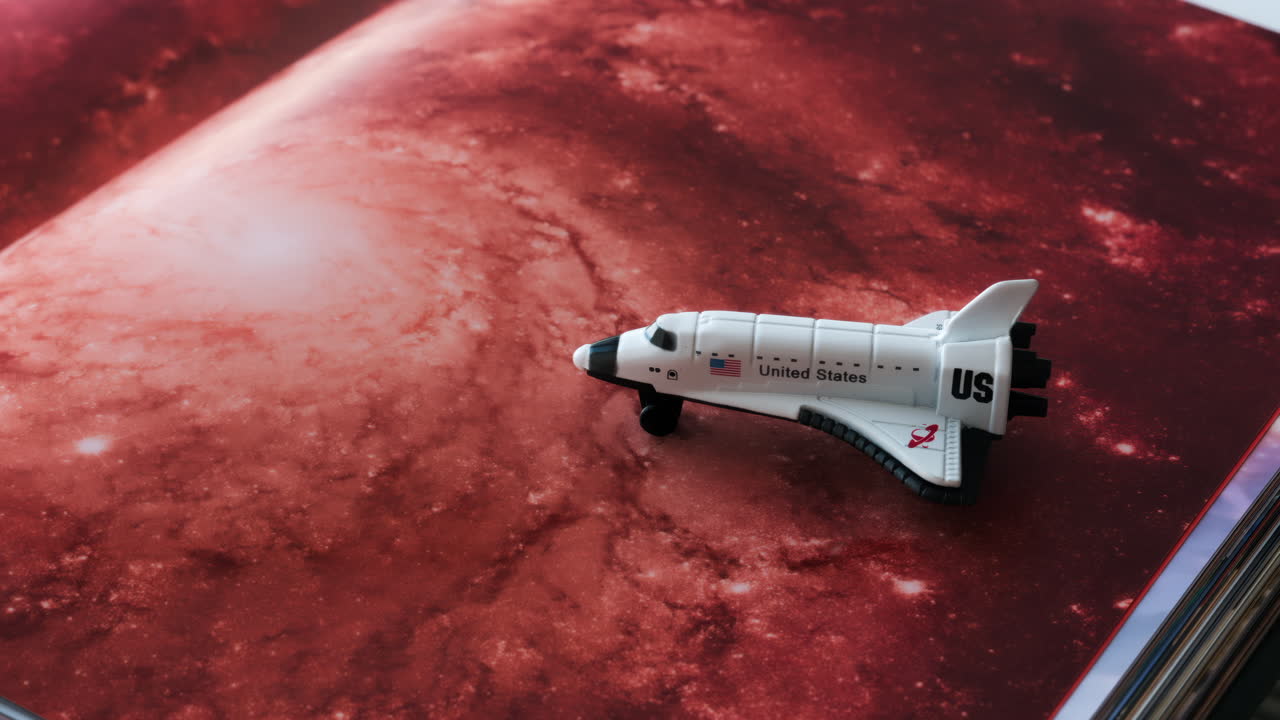 Close up of a miniature toy space shuttle placed on a reddish galaxy background