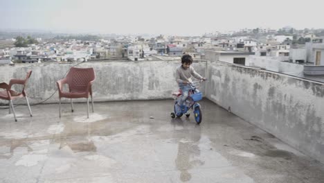 un niño lindo montando en bicicleta en el techo de su casa y disfrutando del ocio durante el día