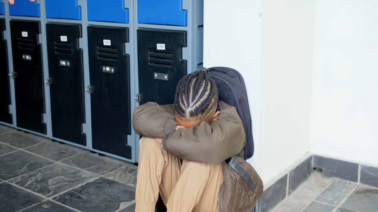Boy sitting by lockers with head down, feeling upset at school