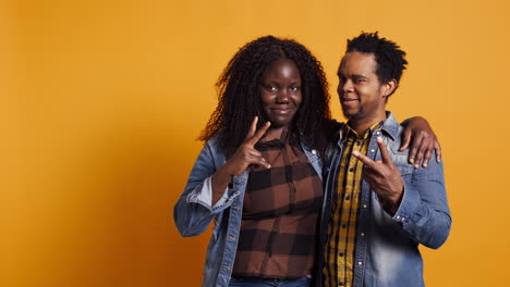 Cute-couple-showing-peace-sign-against-yellow-background