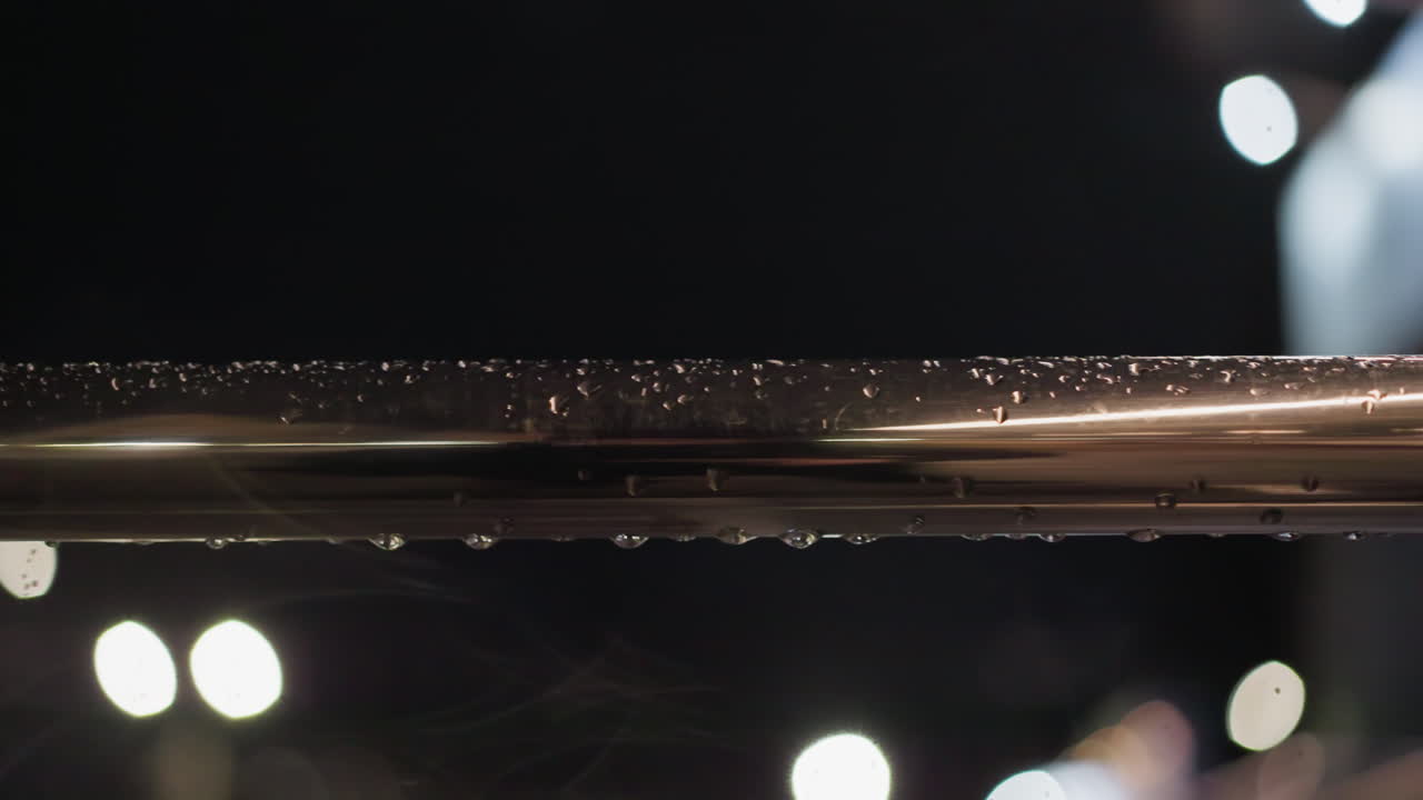vista de cerca de una barandilla de metal empapada de lluvia por la noche, con gotas de agua brillando bajo una iluminación suave