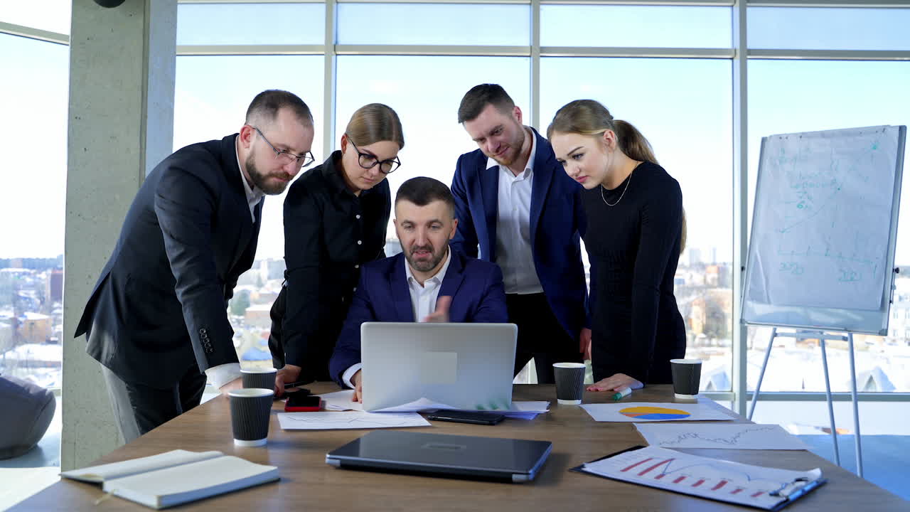 Teamwork of business partners in office. Group of young people in elegant clothes looking into a laptop and discuss business plan together.