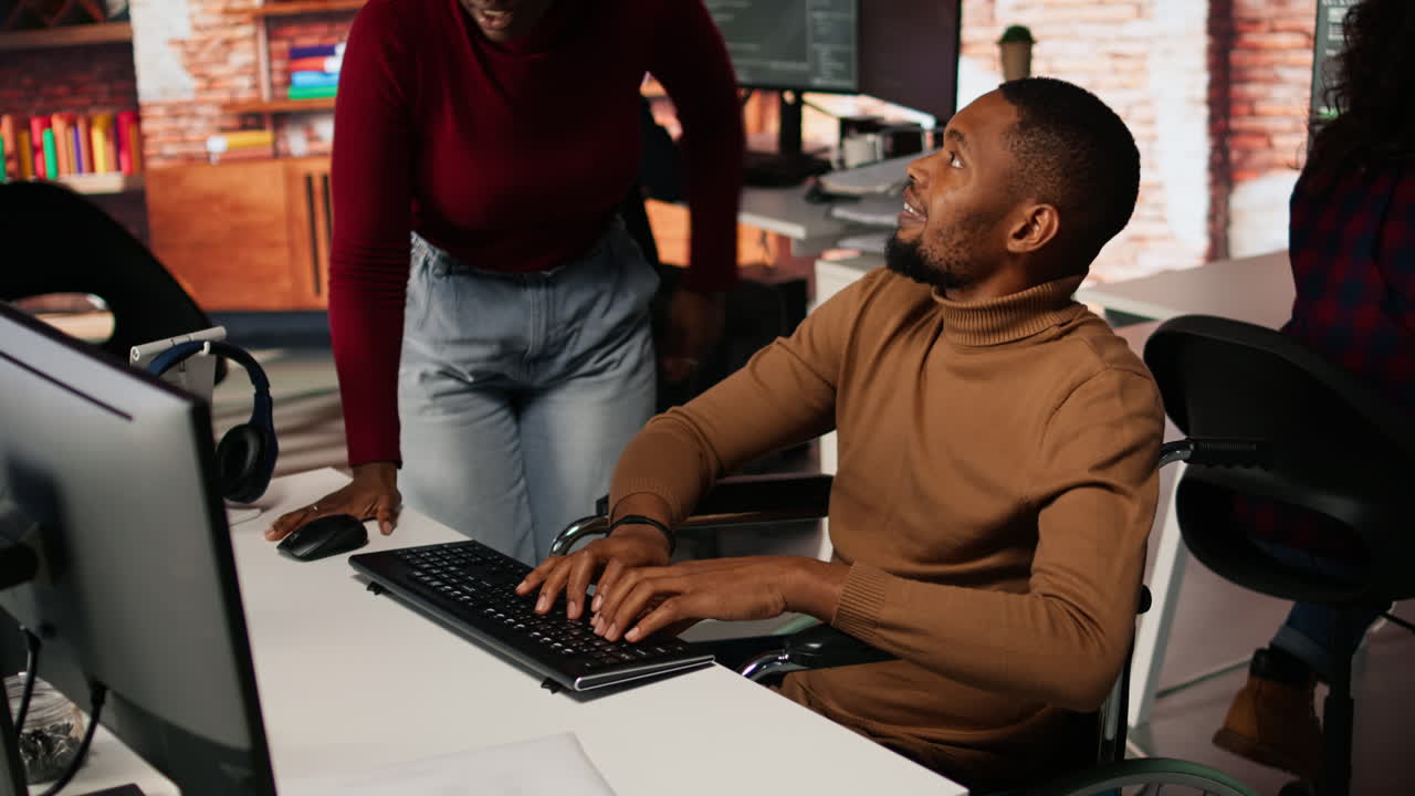 Man with disability typing on PC and chatting with coworker