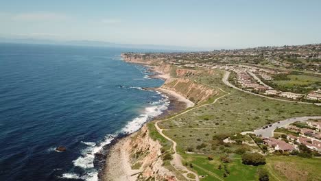 4k aerial view of the pacific ocean with cliffs in palos verdes, los angeles, california on a warm, sunny day with mountains in the background