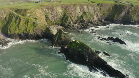 Vista-Aérea,-Dunquin-Pier-Está-Situado-En-Una-Pequeña-Bahía-Aislada-Rodeada-De-Acantilados-Rocosos,-Famosa-Imagen-Postal-De-Irlanda,-El-Paisaje-Circundante-Es-Una-Atractiva-Mezcla-De-Montaña-Y-Acantilado