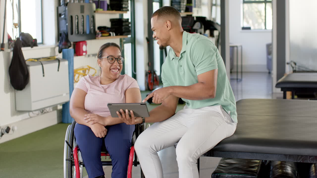 In disability rehab, man showing tablet to woman with paraplegia in wheelchair, both smiling