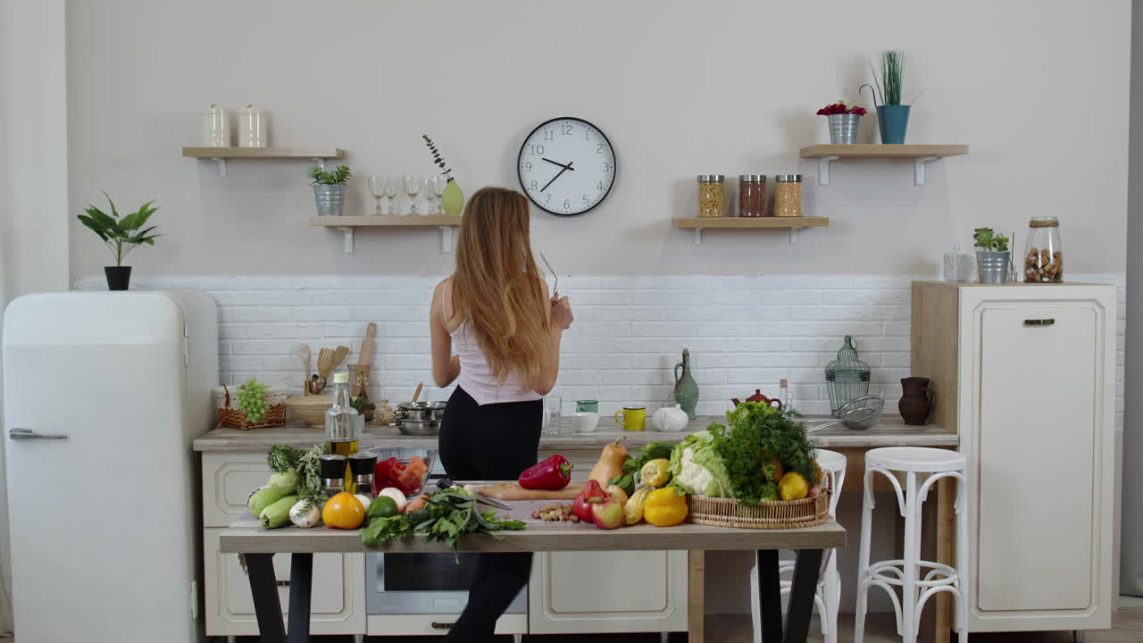 encantadora chica vegana con cabello largo bailando y cantando en la cocina moderna. dieta de alimentos vegetales crudos