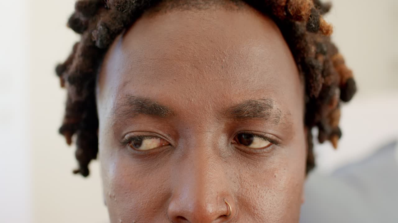 Homme africain à la maison baissant le regard, clignant des yeux, regardant à gauche, se recentrant, anneau nasal, dreadlocks