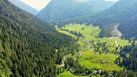 flying over a beautiful valley in northern italy, high in the mountains green healthy grass stretches from one side to the other, a small river flows in the middle