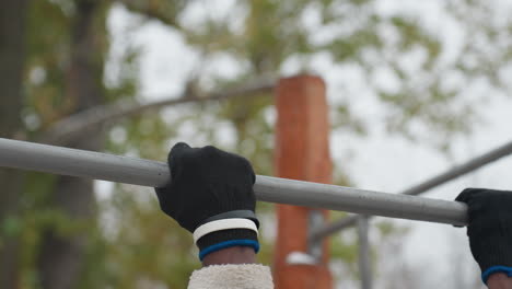 determined young man working out in cold weather, gripping pull-up bar with intensity, wearing black and white wristband on right hand, he focuses on strength training, snowy background