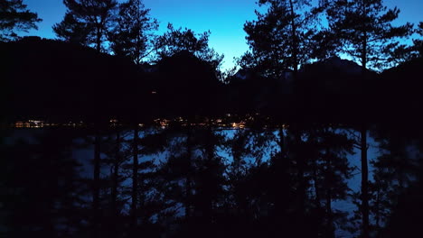 ascending revealing shot of a lakefront village behind trees in tyrol, austria in the evening