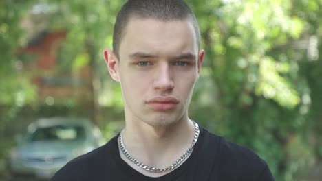 Man-In-Black-T-Shirt-Stepping-Back-While-Looking-At-Camera-With-Blurry-Nature-On-The-Background