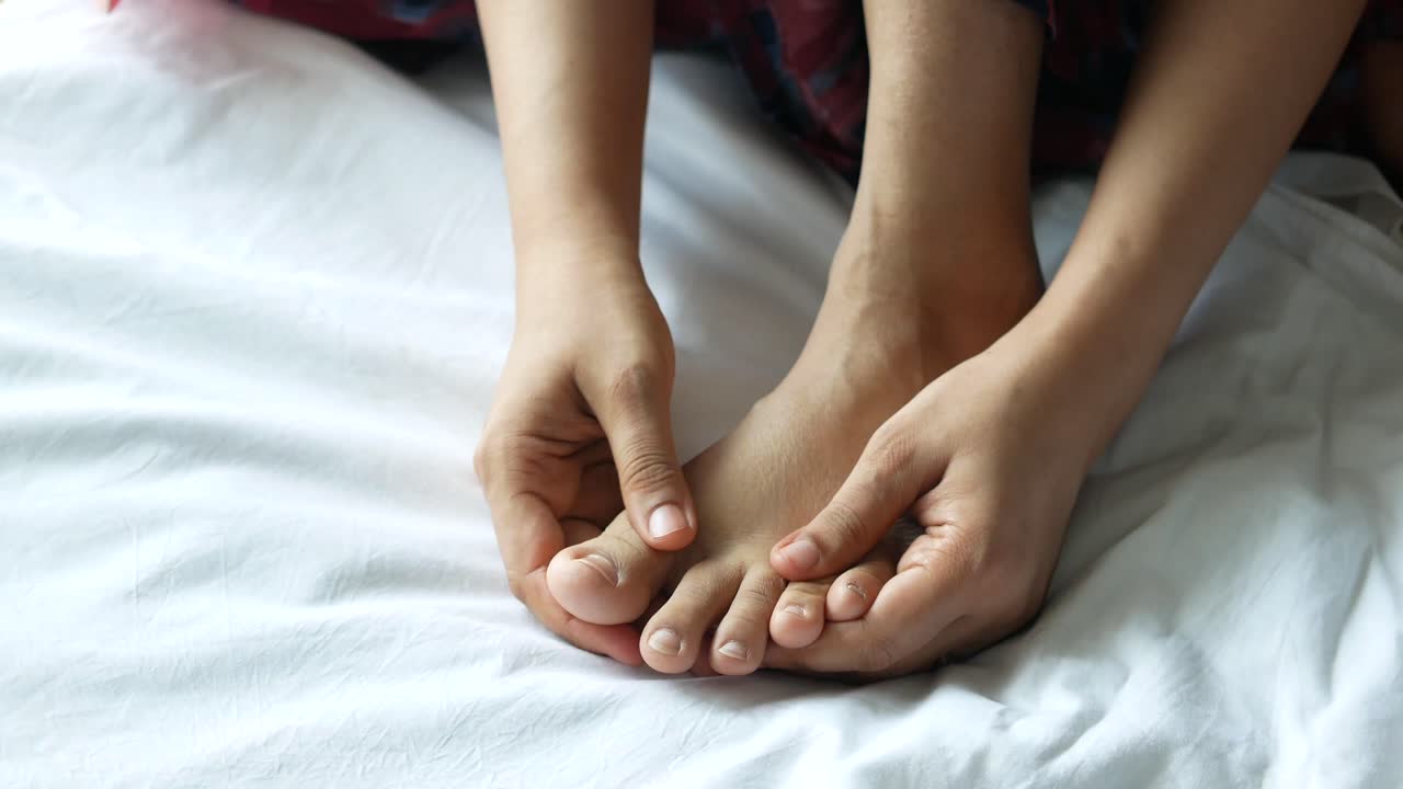 Person Massaging Their Toes on a Bed