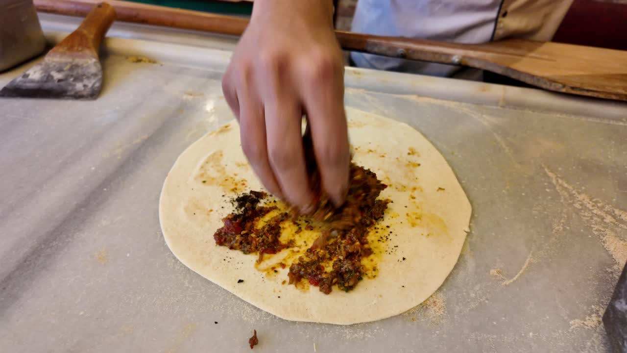 Chef's Hands Spreading Meat Mixture on Flatbread Dough