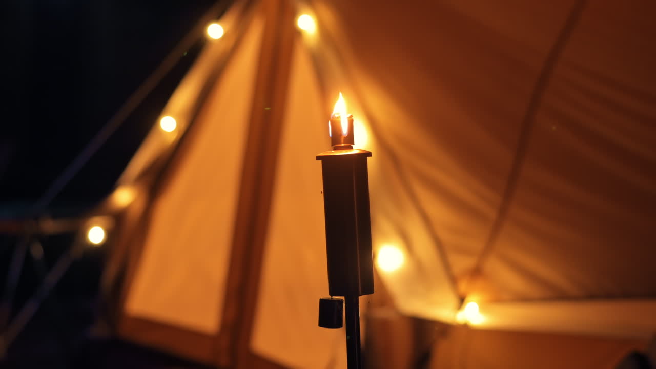 Tenda con torcia e lampade accese in un glamping, di notte