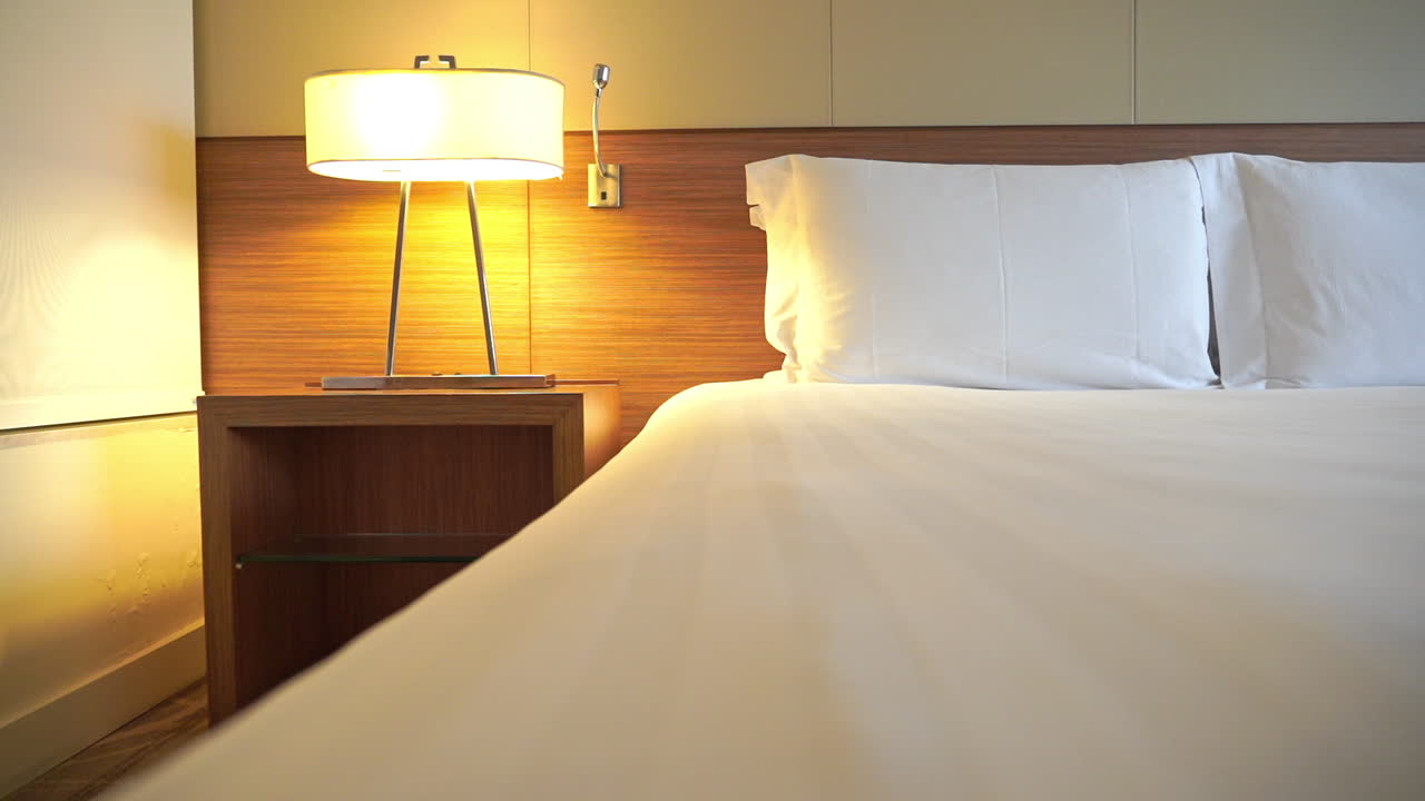 Panning across a hotel suite bed the camera comes to rest on the left side of the bed and nightstand