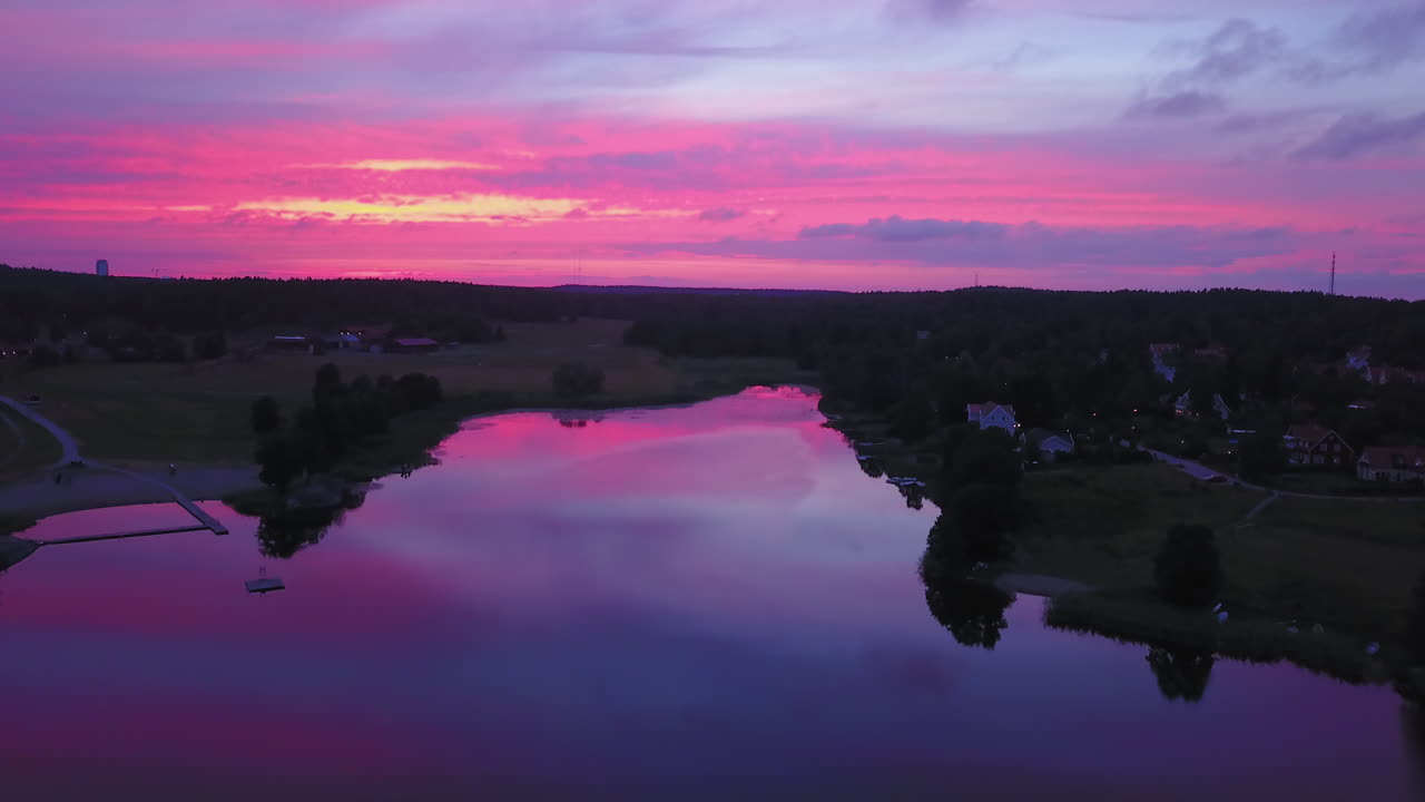 Riprese aeree in discesa, vista con drone all'indietro, sopra un lago e una città, cielo viola, durante un tramonto o crepuscolo dai colori vivaci, ad Albysjon, Tyreso, Svezia