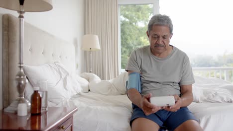 biracial senior man testing blood pressure in bed at home, slow motion