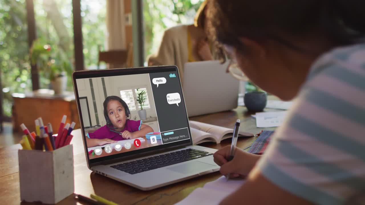 Schoolgirl using laptop for online lesson at home, with her colleague and web chat on screen