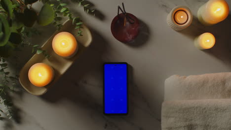 Blick-Von-Oben-Auf-Das-Stillleben-Mit-Bluescreen-Handy-beleuchteten-Kerzen-Und-Räucherstäbchen-Mit-Grüner-Pflanze-Und-Handtüchern-Als-Teil-Der-Spa-Tagesdekoration