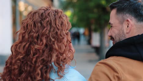 rear view of caucasian man and redheaded woman talking and walking down the street