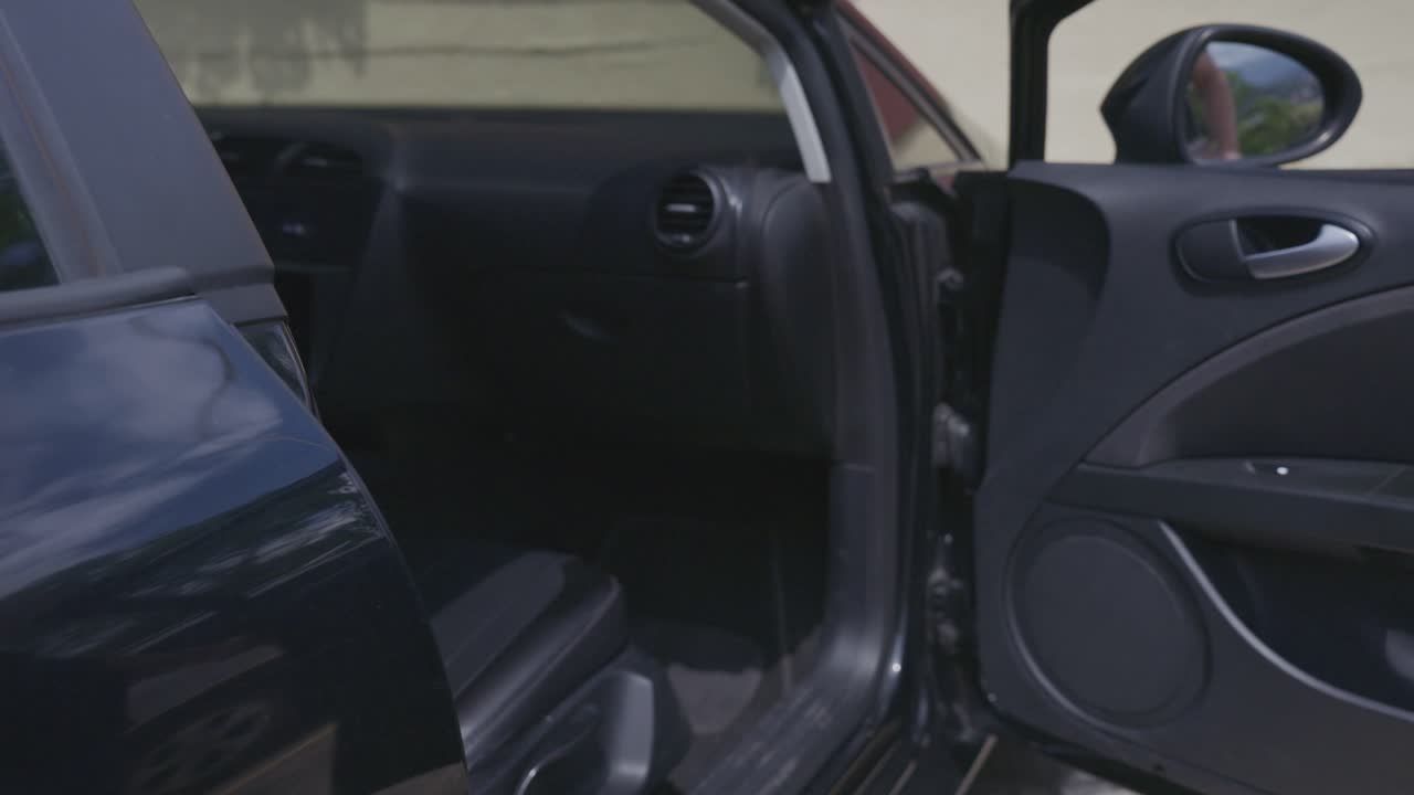 Vista laterale posteriore di un uomo che apre la portiera del conducente e si siede in un'auto nera, preparandosi a guidare.