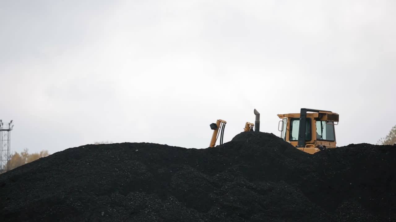 Coal mining industry and transportation. Yellow tractor riding at coal warehouse for transportation